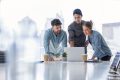 Business team working on a laptop computer. Three people are wearing  casual clothing. They are standing in a board room. Multi ethnic group with Caucasian and Latino men and women